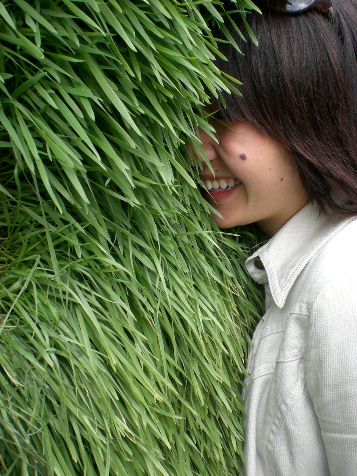 Picture of Lian Chikako Chang smiling, with her face buried in a wall of well-kept green grass.