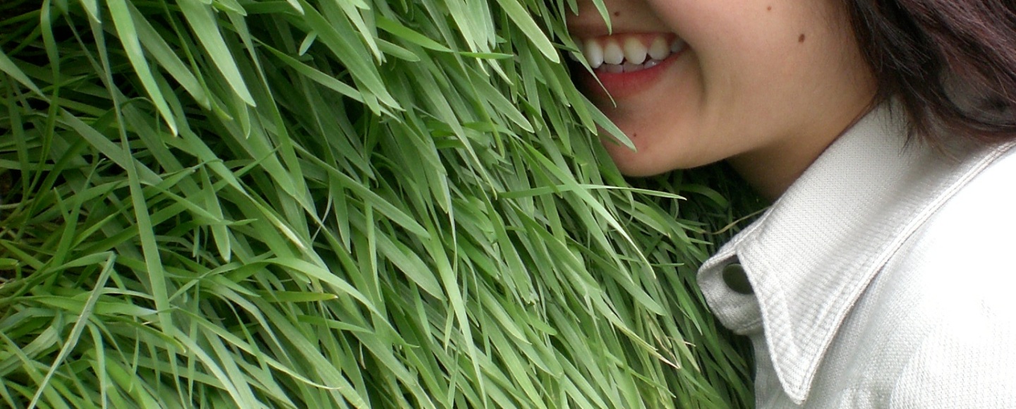 Picture of Lian Chikako Chang smiling, with her face buried in a wall of well-kept green grass.